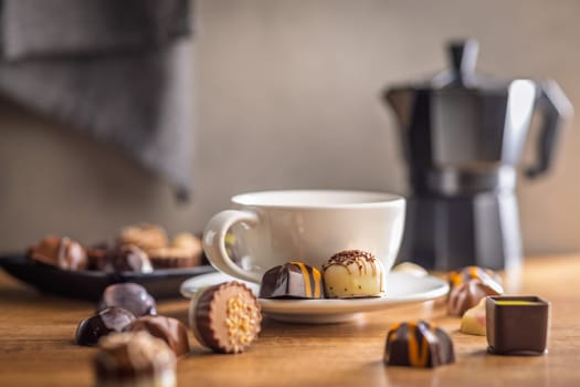 Mix of chocolate pralines and coffee cup on a wooden table.