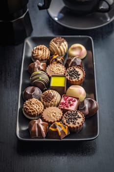 Mix of chocolate pralines on plate on a black table.