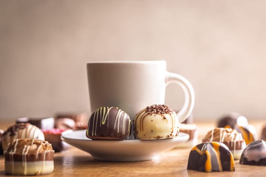 Mix of chocolate pralines and coffee cup on a wooden table.