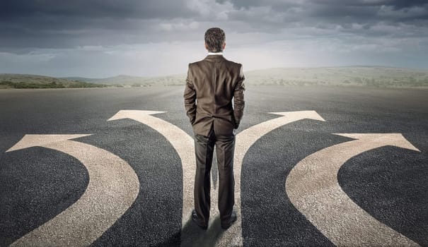 Doubtful businessman choosing the way as multiple arrows on the road show different directions. Choose the correct pathway, the right choice and difficult decision concept