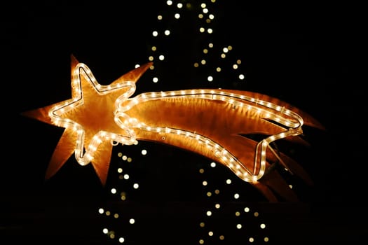 A shining poinsettia in front of the blurred lights of a Christmas tree