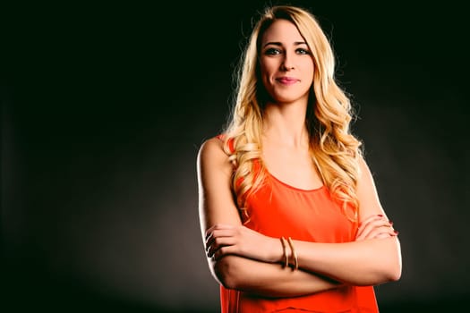 Confident young woman with folded arms against a black background, radiating professionalism and elegance in her orange dress, embodying strength and ambition