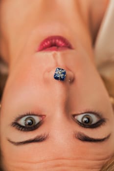 Young woman lying down with a small blue gift placed under her nose, expressing surprise and curiosity in a playful and intriguing composition