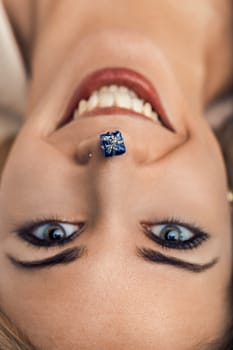 Cheerful young woman with dark hair and blue eyes holds a miniature blue gift box on her nose. Expressing joy and excitement. Possibly symbolizing the anticipation of receiving or giving a present