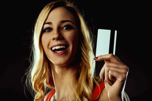 Excited young woman showing a generic credit card with a magnetic stripe and blank space for adding design or text, on a dark background