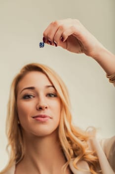 Young blonde woman holding a small gift box between her fingers, representing emotions, feelings and related concepts, in a studio shot with a neutral background