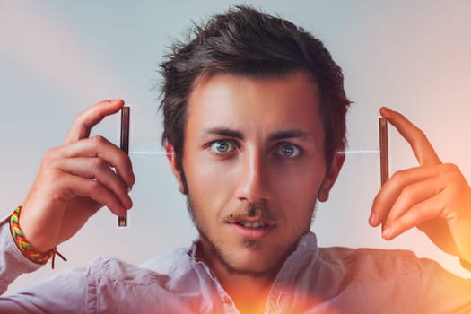 Young adult man experiencing sound waves emanating from two metal bars held near his ears, showcasing a surprised expression while engaging in a moment of curiosity and discovery