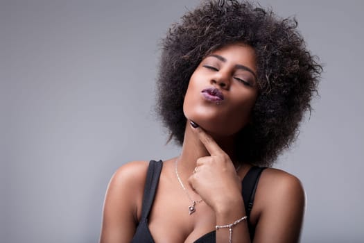 Studio portrait of a beautiful young woman sending a kiss, wearing a black top and silver jewelry, her eyes are closed and she has an afro hairstyle