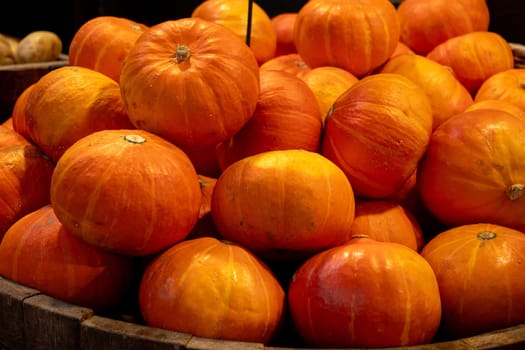 A pile of orange pumpkins in a wooden crate. The pumpkins are all different sizes and shapes, but they all have a similar color and texture. The crate is rustic