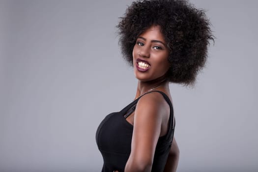 Studio portrait of a cheerful young african american woman with an afro hairstyle, wearing a black top, looking at the camera with a playful smile, expressing confidence and happiness