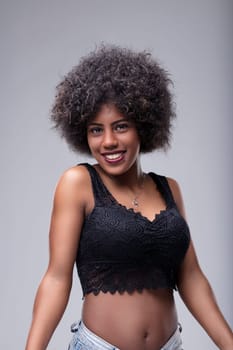 Studio portrait of a beautiful young woman with an afro hairstyle smiling confidently at the camera, showcasing her unique style and positive attitude