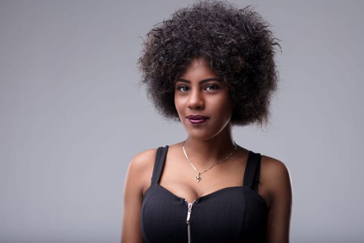 Studio portrait of a beautiful young woman with an afro hairstyle, wearing a black top and silver necklace, looking at the camera with a confident expression