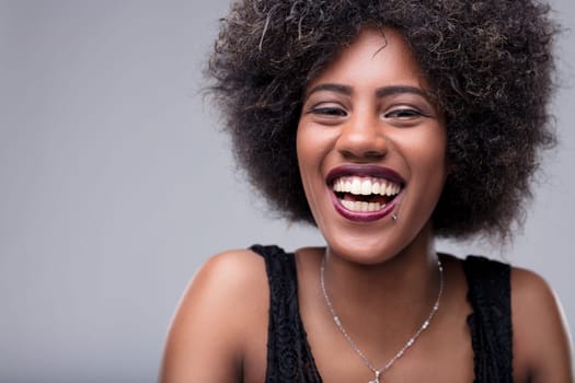 Studio portrait featuring a cheerful young woman with afro hair, smiling broadly and revealing her teeth, radiating happiness and joy in a vibrant expression