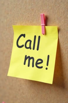 A bright yellow sticky note with bold black text invites someone to call. It is securely pinned to a corkboard, conveying a sense of urgency and communication in a simple yet effective way.
