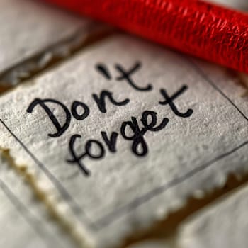 A close-up view of a handwritten note with the words Don't forget prominently displayed on textured paper, accompanied by a bright red string, emphasizing the importance of remembering tasks.
