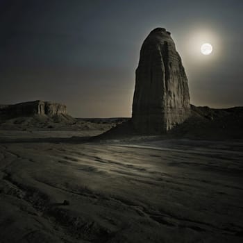 A dramatic landscape featuring a tall rock formation under a full moon in a desolate desert at night. A high-quality AI-generated photo.