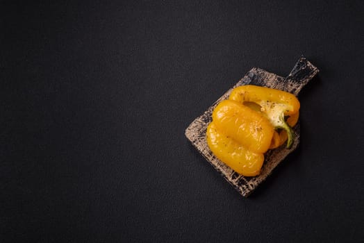 Yellow sweet pepper cut in half and grilled with salt, spices and herbs on a dark concrete background
