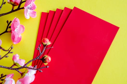 Top view of Chinese New Year with pink flower decoration with red packets on yellow cover background with customizable space for text. Chinese New Year celebration.