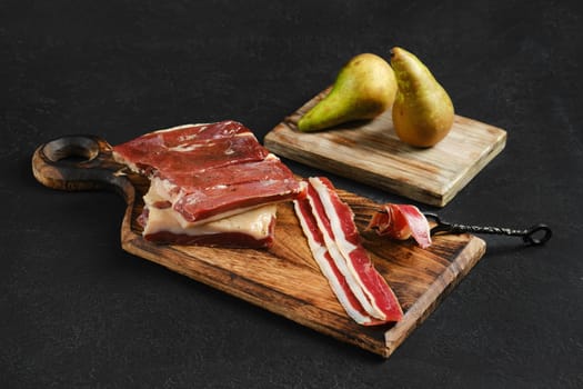 A beautifully arranged charcuterie board displays thinly sliced cured duck meats alongside fresh pears on a rustic wooden surface