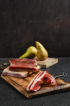 Slices of rich cured duck meat on rustic wooden cutting boards alongside ripe pears. The warm lighting and dark background enhance the appetizing presentation of this culinary arrangement.
