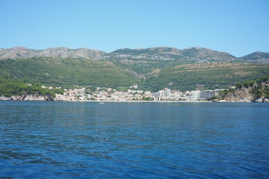 Petrovac, Montenegro 07.22.24 A boat ride past shore with vacationers, sunbathers and swimmers. Hotels, sun umbrellas, Adriatic waves, buoys. Beach tourism. Vacation travel. Summer day. Sandy pebble.