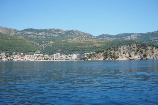Petrovac, Montenegro 07.22.24 A boat ride past shore with vacationers, sunbathers and swimmers. Hotels, sun umbrellas, Adriatic waves, buoys. Beach tourism. Vacation travel. Summer day. Sandy pebble.