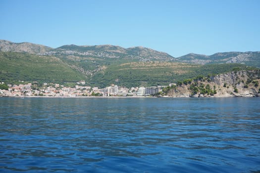 Petrovac, Montenegro 07.22.24 A boat ride past shore with vacationers, sunbathers and swimmers. Hotels, sun umbrellas, Adriatic waves, buoys. Beach tourism. Vacation travel. Summer day. Sandy pebble.