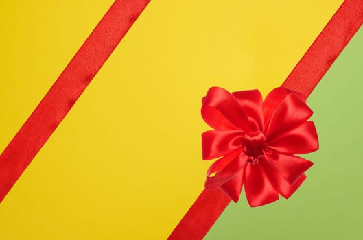 Tied bow made of red silk ribbon on green yellow background, decor for a gift