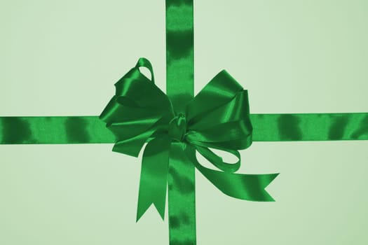 Green silk ribbon bow and cross ribbons on a green background, gift wrapping. Top view