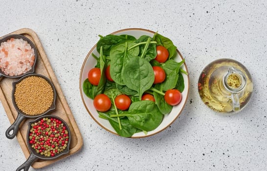 Salad of spinach leaves and cherry tomatoes in a round white plate on a white background, top view