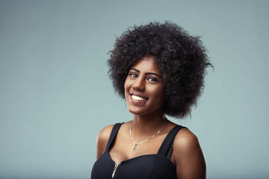 Studio portrait of a cheerful young latin american woman with curly hair, smiling confidently and expressing happiness against a light blue background