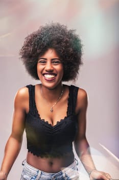 Portrait of a cheerful young woman with curly afro hair, beaming with a big smile while wearing a stylish black top and jeans, engaging directly with the camera
