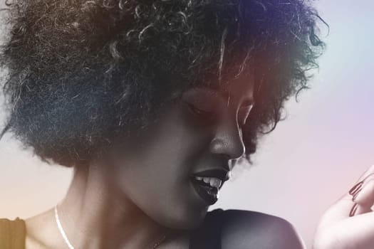 Black and white portrait featuring a young woman with an afro hairstyle, posing in a studio illuminated by colorful light effects, looking down and radiating a joyful smile