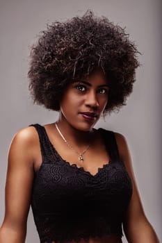Portrait of a beautiful young african american woman with curly hair and dark skin wearing a black top and silver necklace, looking directly at the camera with a confident expression