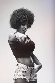 Black and white portrait featuring a young woman with striking afro hair, confidently pointing her finger while engaging directly with the camera, exuding self-assuredness and style