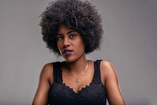 Studio portrait of beautiful young african american model with afro hairstyle wearing black lacy top and silver necklace looking confidently at camera against gray background