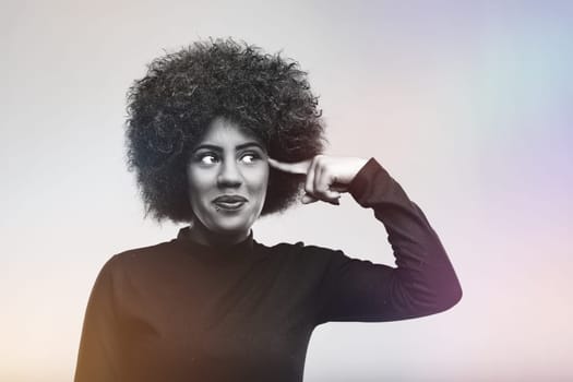 Studio portrait of a young woman pointing her finger to her temple suggesting she is crazy or has a brilliant idea, looking up with a funny expression