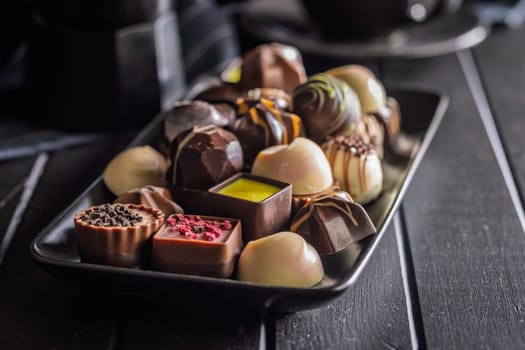 Mix of chocolate pralines on plate on a black table.