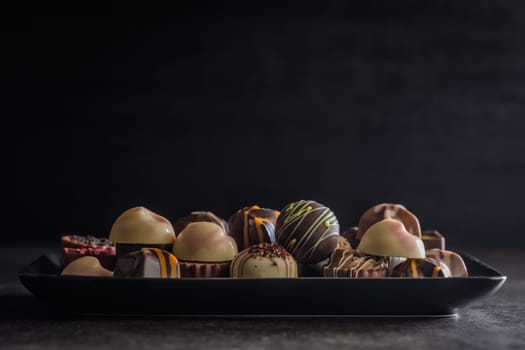 Mix of chocolate pralines on plate on a black table.