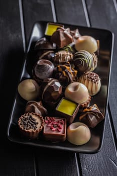 Mix of chocolate pralines on plate on a black table.