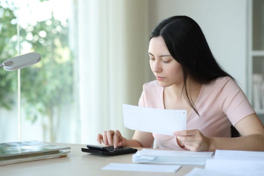 Serious asian woman calculating expenses holding invoices at home