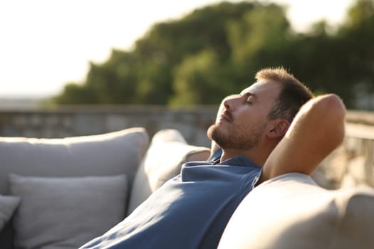 Side view portrait of a relaxed man resting sitting on an exterior sofa in a house or hotel terrace