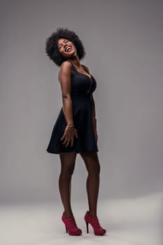 Studio shot of a cheerful latin american woman with afro hair wearing a black dress and red high heels, laughing and enjoying herself, expressing freedom and confidence