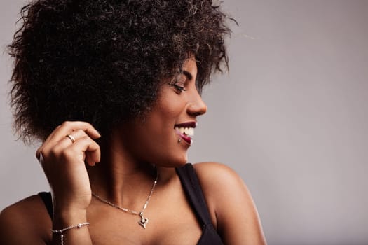 Smiling latin american woman with curly hair, touching her hair and gazing away, radiating freedom and confidence in a stylish studio portrait against a gray background