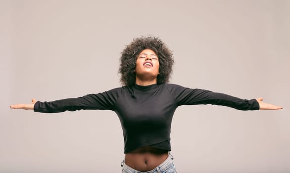Young latin american woman with curly hair, wearing a black long-sleeved shirt and jeans, is expressing freedom and happiness with open arms and closed eyes, feeling like a diva