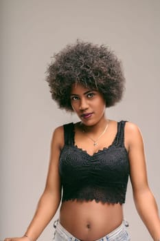 Young latin american woman with afro hair looking at camera, expressing confidence and freedom while wearing a black top and jeans, representing diversity, beauty, and female empowerment