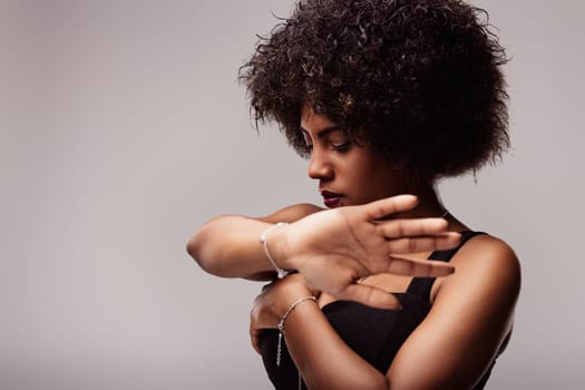 Studio portrait of a young latin american woman with curly hair, wearing a black top and bracelets, expressing confidence and freedom through her elegant pose and captivating gaze