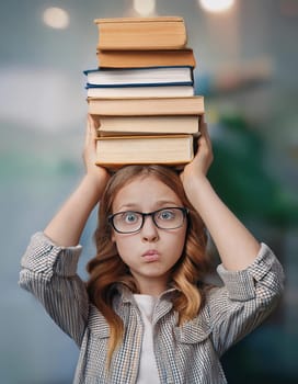 Fatigue pupil girl holds a pile of books on her head looks confused and bewildered due high volume of homework. Teenage student tired of difficult educational system