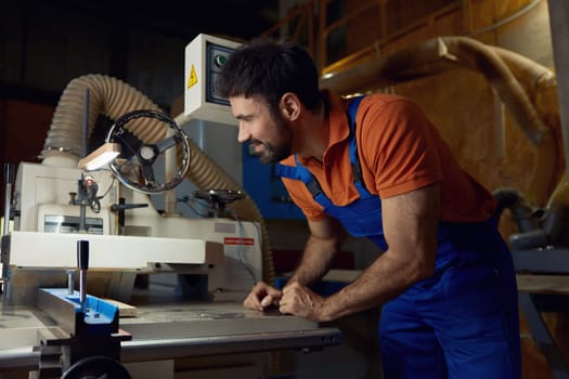 Woodworker using planer machine for production wooden materials specific size. Taking into account thickness to perform high-precision cutting into blanks for furniture at carpentry shop