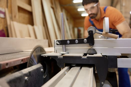Man professional carpenter wearing workwear using jointer equipment for final processing of wood plank. Furniture production industry and woodworking concept